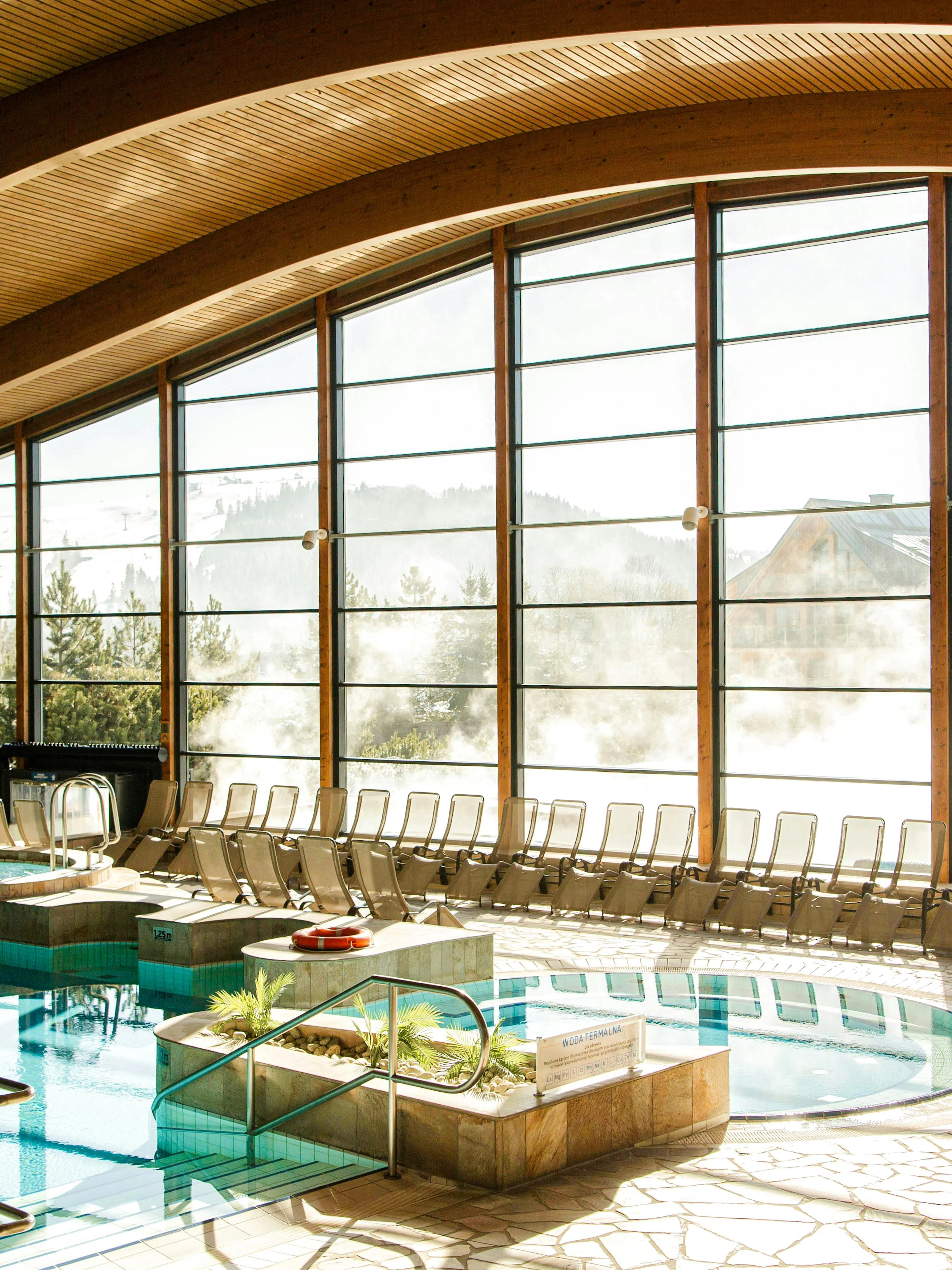 Indoor pool area at Terma Bania in Białka Tatrzańska with large windows and lounge chairs.