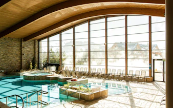 Indoor pool area at Terma Bania in Białka Tatrzańska with large windows and lounge chairs.