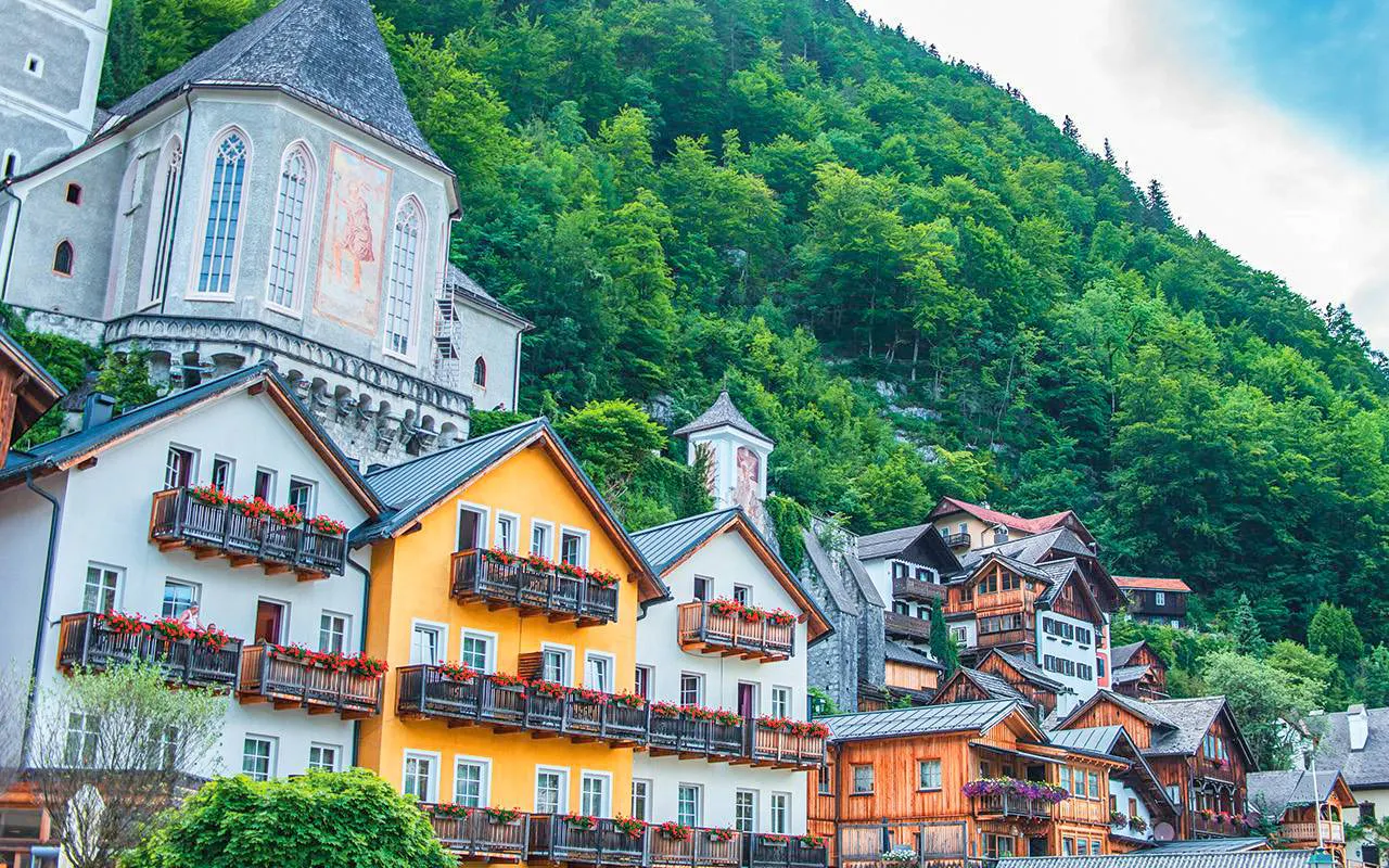 Colorful houses and church in Hallstatt village, Austria, surrounded by lush green hills.