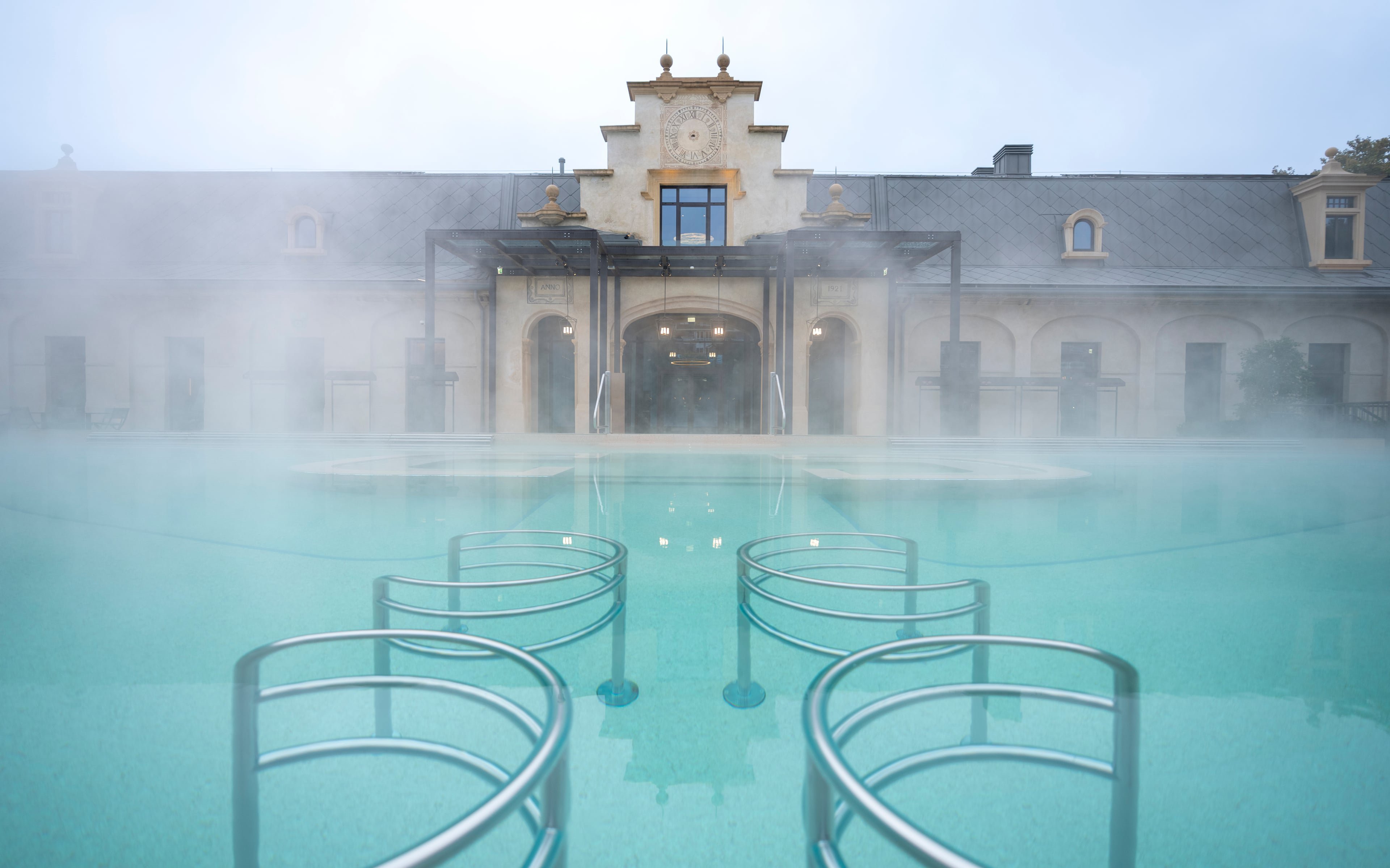 Milan spa with steaming hot pool and historic building in daylight.