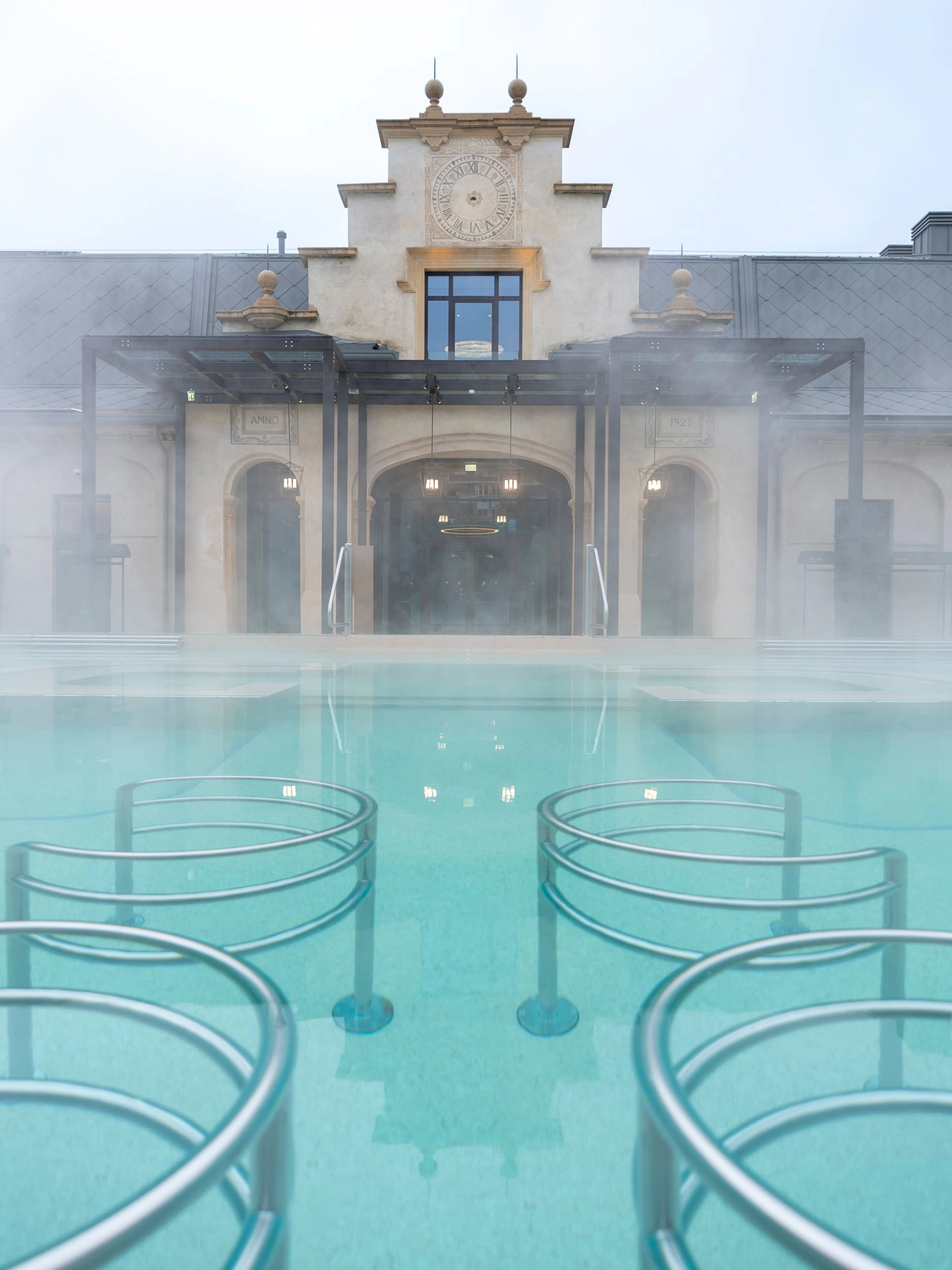 Milan spa with steaming hot pool and historic building in daylight.