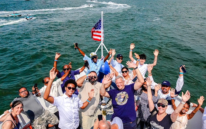 Guests enjoying the Statue of Liberty and NYC landmarks cruise, waving on a boat.