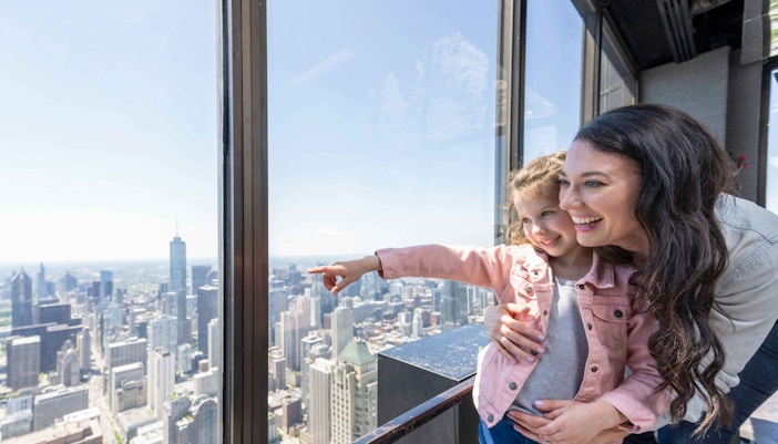 Visitors enjoying panoramic views from 360 Chicago Observation Deck, overlooking Lake Michigan and city skyline.
