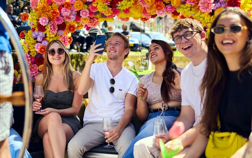 Group enjoying Amsterdam canal cruise on a flower-adorned boat.