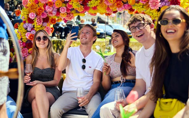 Group enjoying Amsterdam canal cruise on a flower-adorned boat.