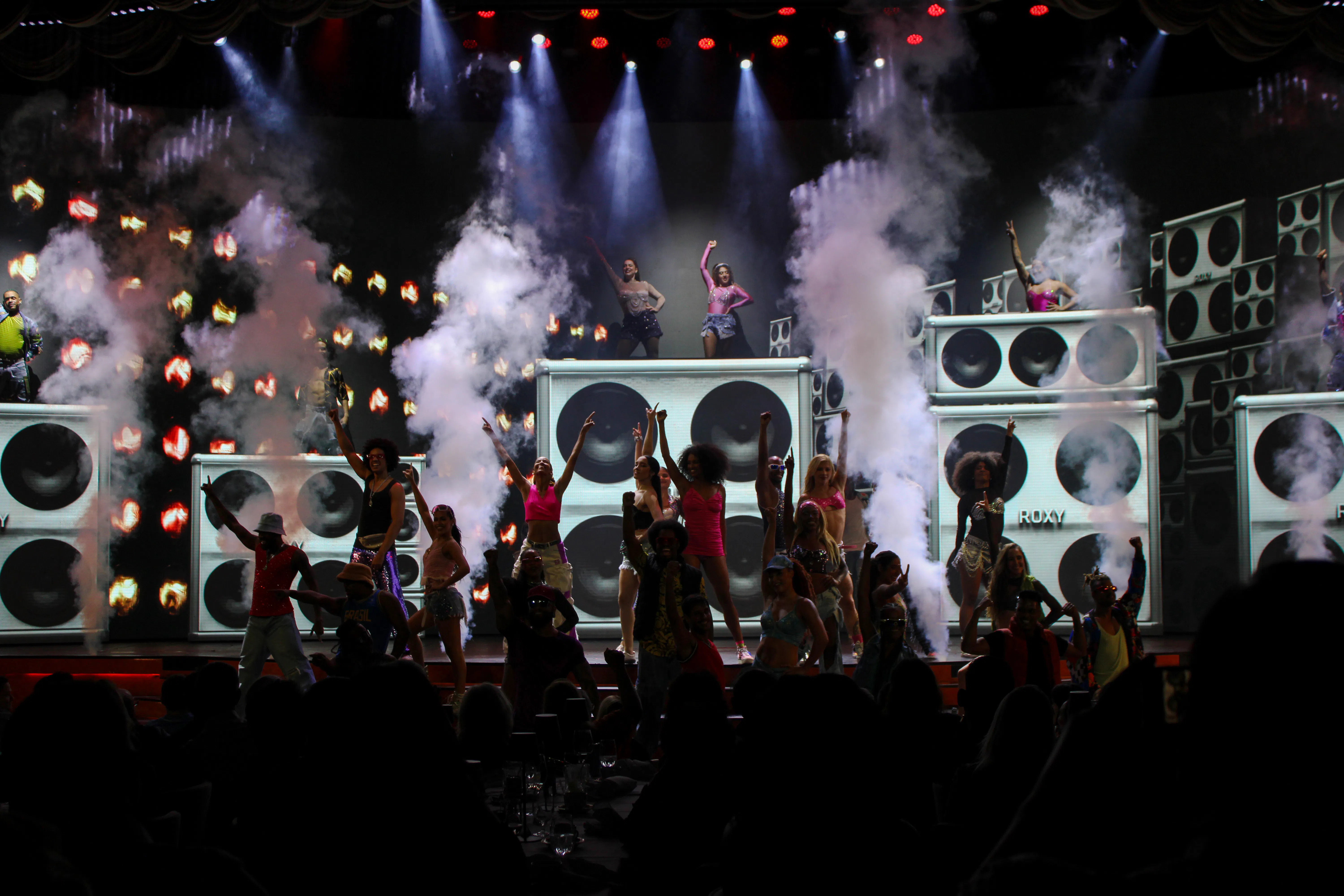 Performers on stage at Roxy Dinner Show, Rio de Janeiro, with vibrant lights and smoke effects.