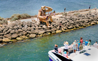 Tourists on boat viewing giant sculpture on Giant & Dolphin Sightseeing Cruise.