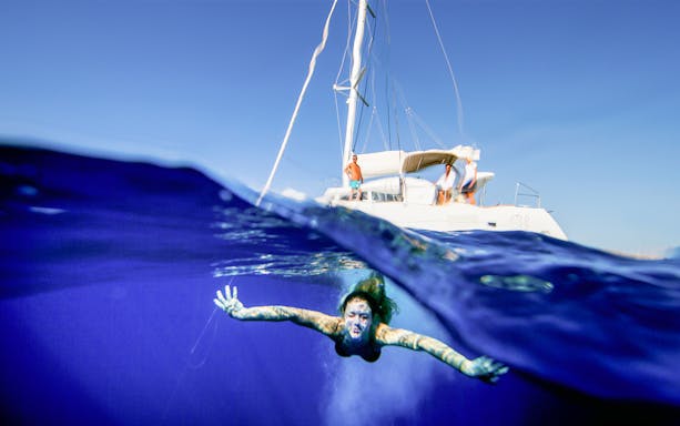 Person swimming near a sailboat during a Semi Private Comfort Day Cruise.