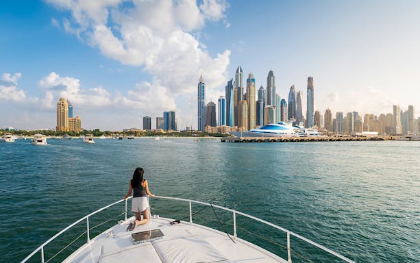 Yacht cruising in Dubai Marina with city skyline in the background.