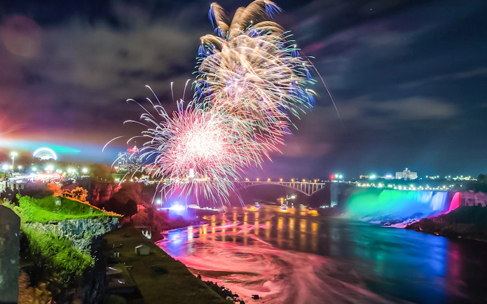 Fireworks display over Niagara Falls, Canada, with illuminated waterfall and bridge.