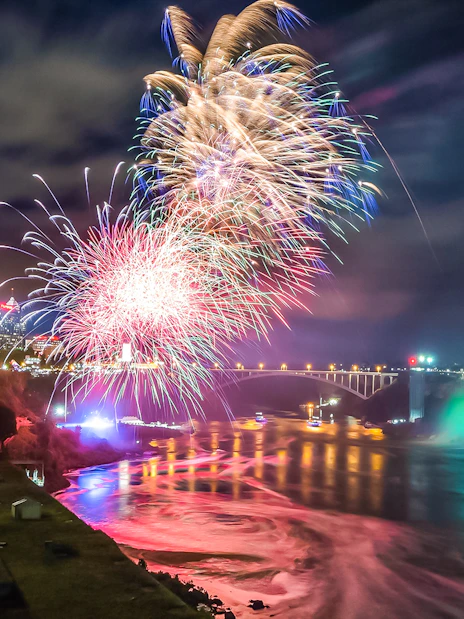 Fireworks display over Niagara Falls, Canada, with illuminated waterfall and bridge.