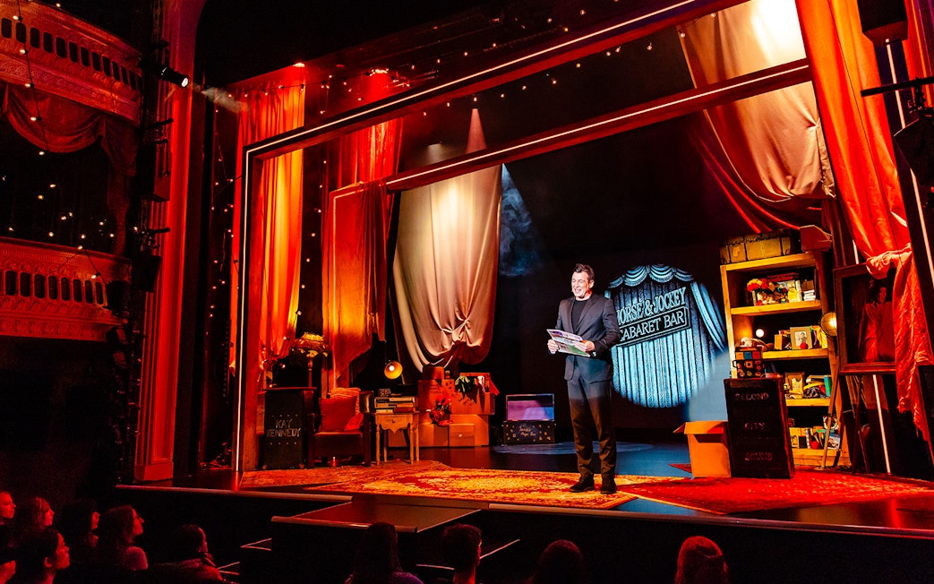Theatre performance of Jamie Allan's Amaze with magician on stage holding a newspaper.
