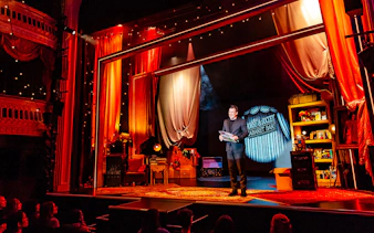 Theatre performance of Jamie Allan's Amaze with magician on stage holding a newspaper.