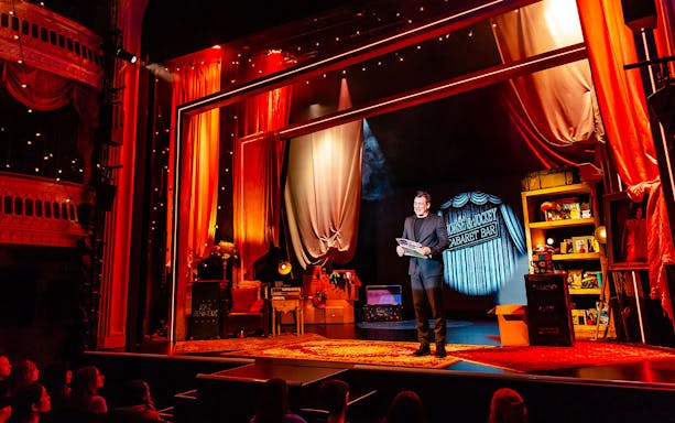 Theatre performance of Jamie Allan's Amaze with magician on stage holding a newspaper.