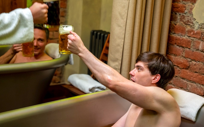 Men enjoying beer in a spa bath, raising mugs in a toast.