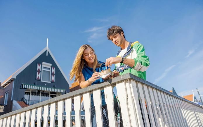 Tourists enjoying stroopwafels on a bridge in a Dutch village.