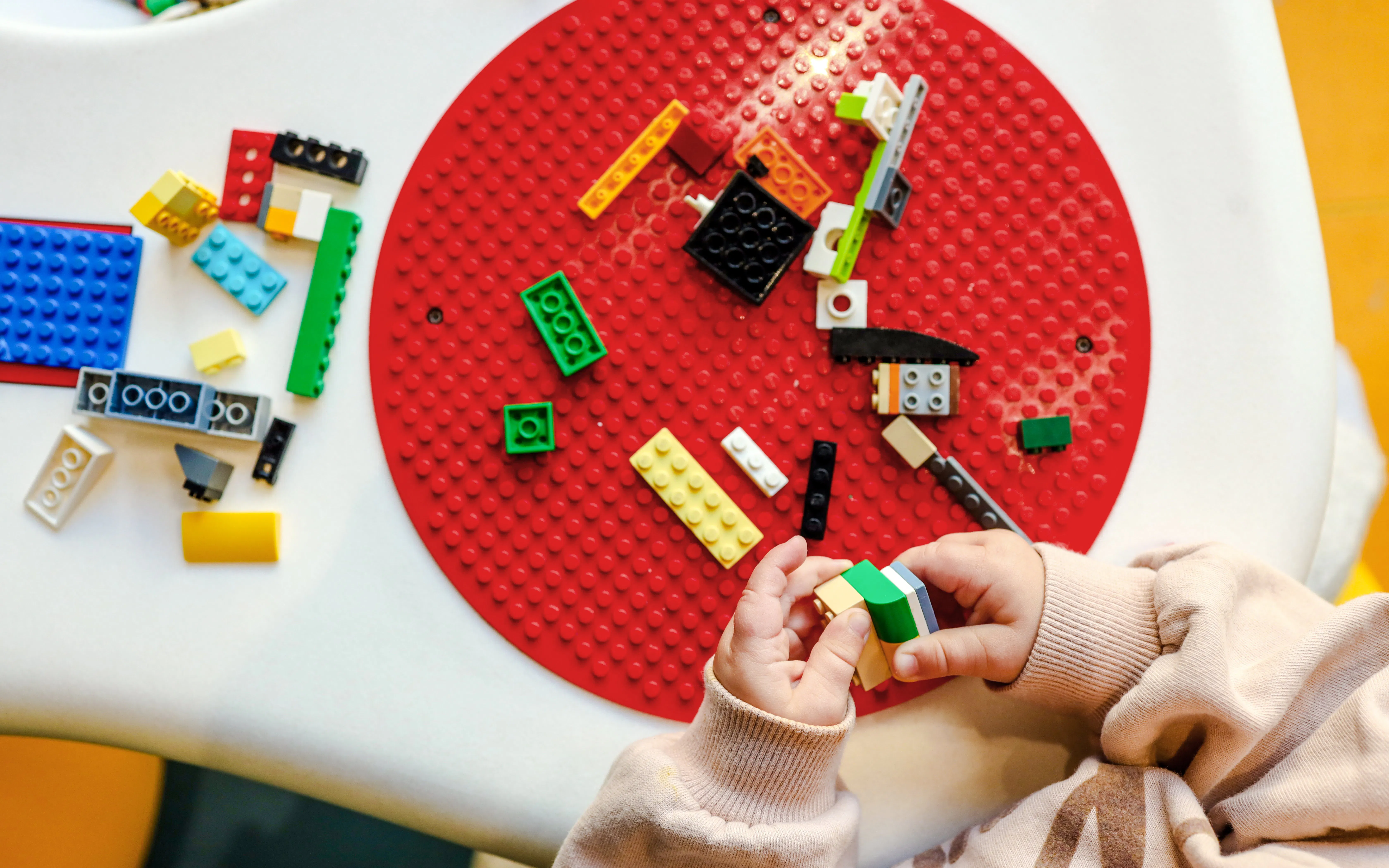 Child assembling colorful blocks on a red circular baseplate.