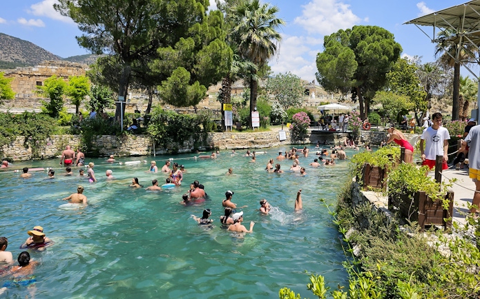 Guests enjoying a swim in Cleopatra's Pool, Pamukkale, surrounded by lush greenery.