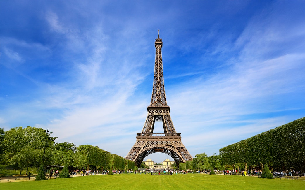 Eiffel Tower with tourists gathered for guided climb to second floor via stairs.