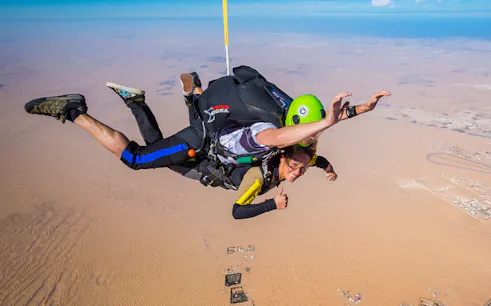Skydivers tandem jumping over desert landscape at drop zone.