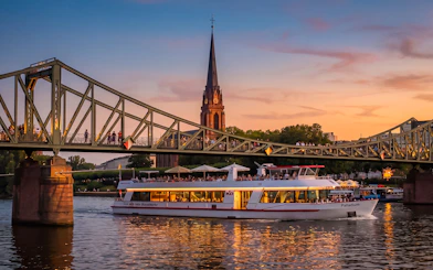 Frankfurt evening cruise boat passing under Iron Bridge at sunset.