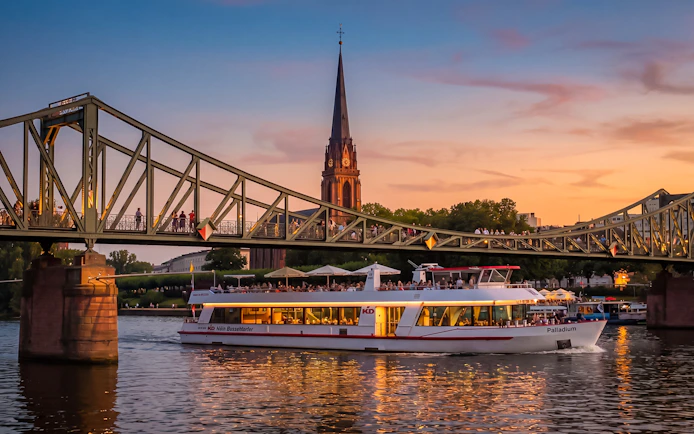 Frankfurt evening cruise boat passing under Iron Bridge at sunset.