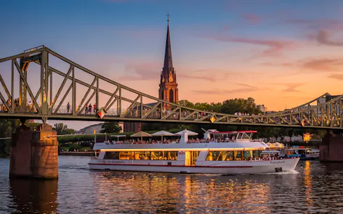 Frankfurt evening cruise boat passing under Iron Bridge at sunset.