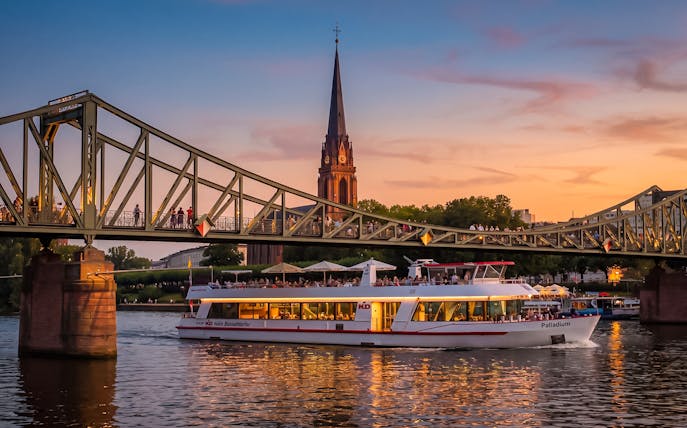 Frankfurt evening cruise boat passing under Iron Bridge at sunset.