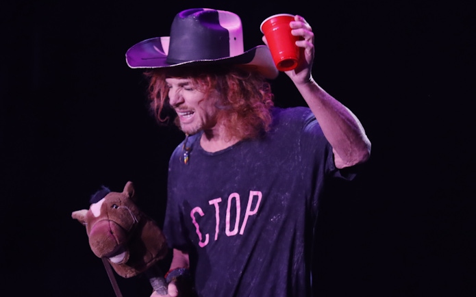 Performer at Carrot Top Vegas show holding a red cup and a toy horse.