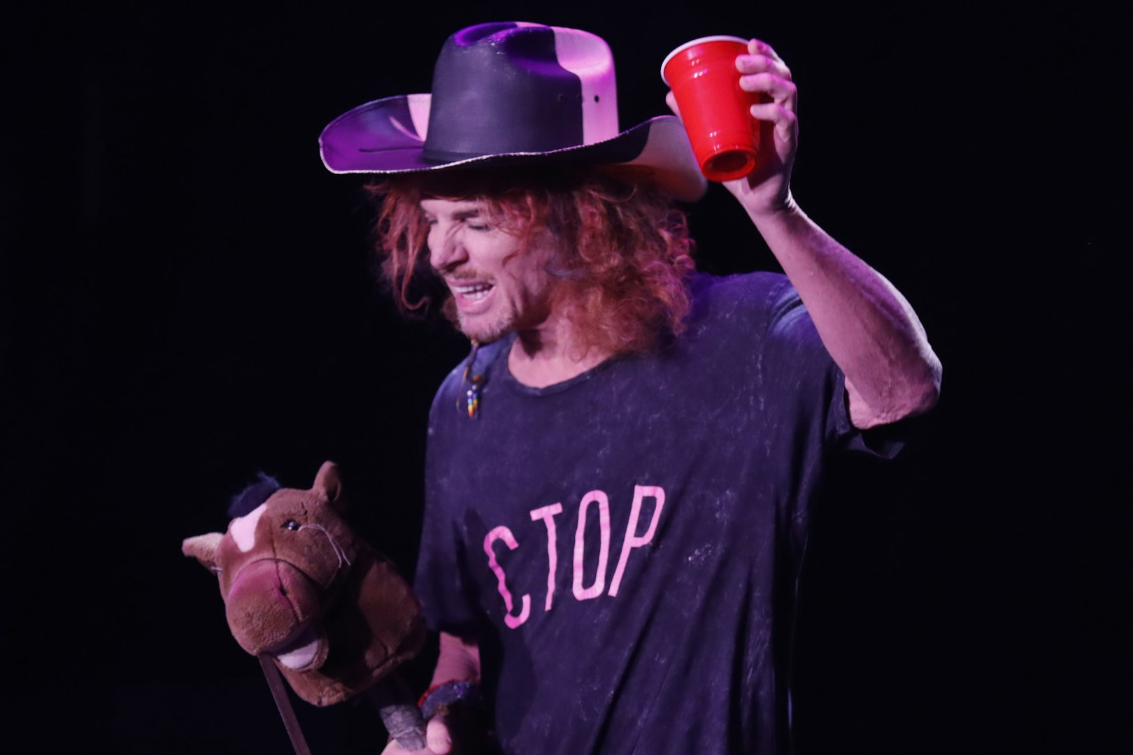 Performer at Carrot Top Vegas show holding a red cup and a toy horse.