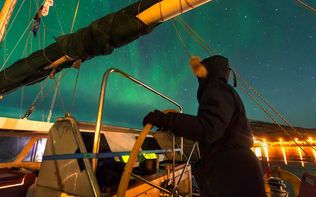 Person steering a boat under the Northern Lights near Reykjavik.