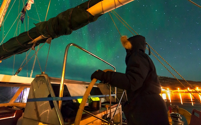 Person steering a boat under the Northern Lights near Reykjavik.