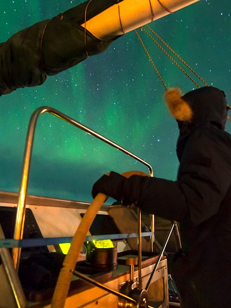 Person steering a boat under the Northern Lights near Reykjavik.