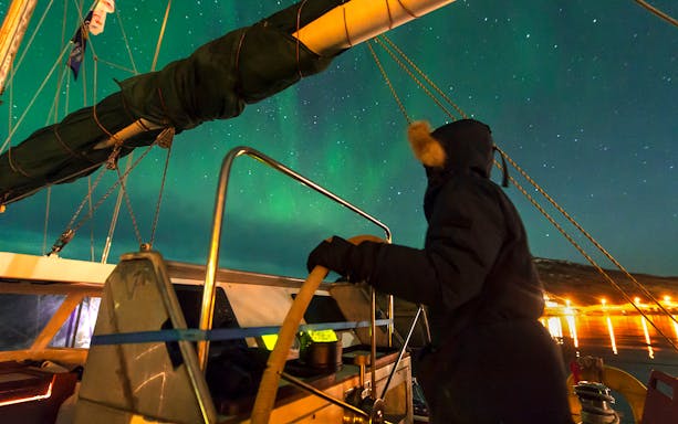 Person steering a boat under the Northern Lights near Reykjavik.
