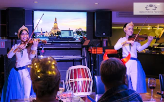 Violinists performing on Chao Phraya Princess New Year's Eve Dinner Cruise with Wat Arun backdrop.