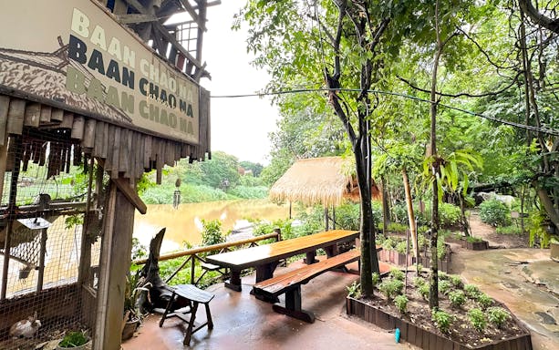 Mae Ping River view with rustic seating area and lush greenery at Baan Chao Na.