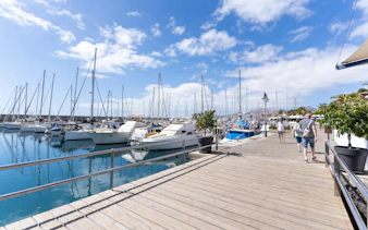 Boats docked at Puerto Calero marina with people walking along the boardwalk, Lanzarote.