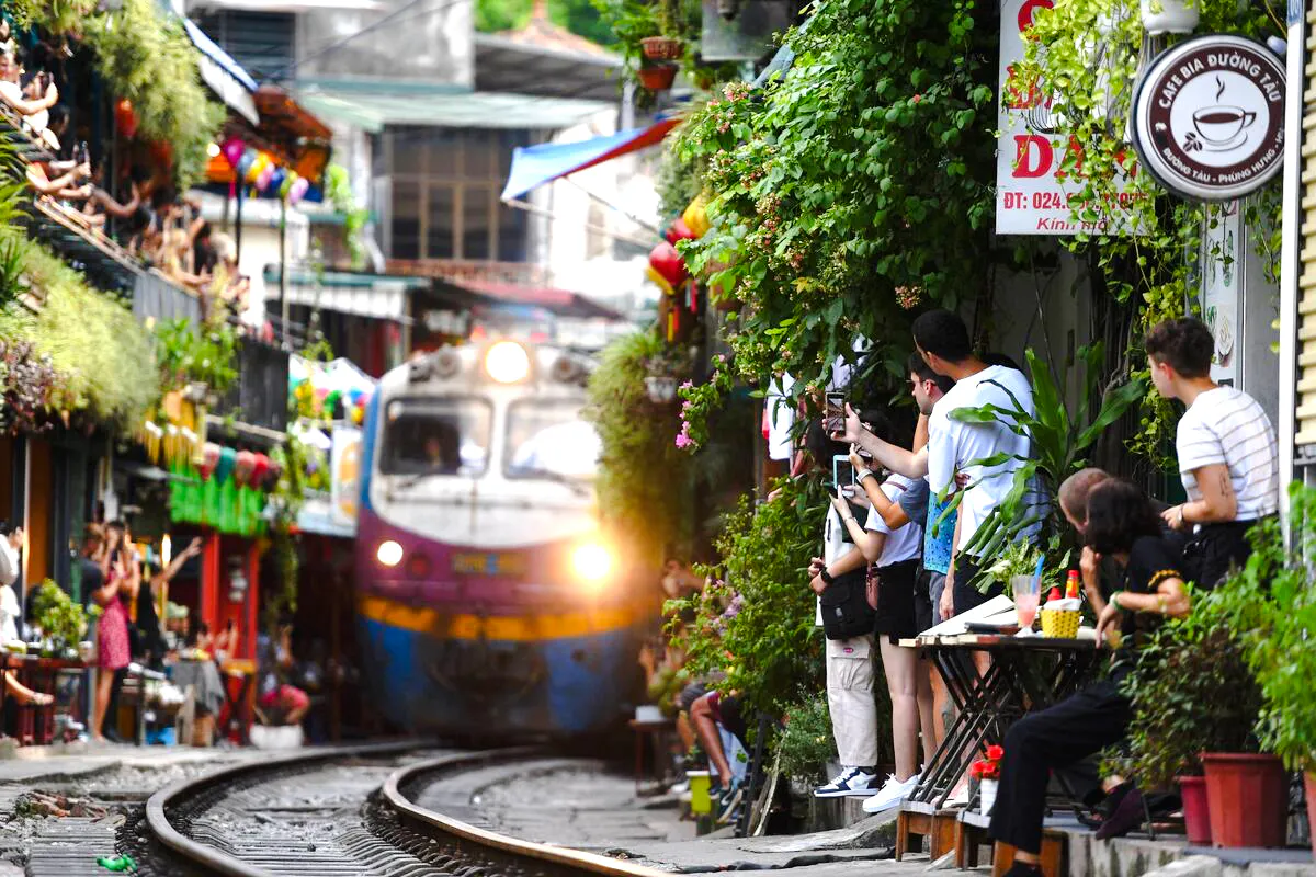 Train passing through Hanoi's Train Street with tourists capturing photos, Hanoi Photo Tour on Vespa.