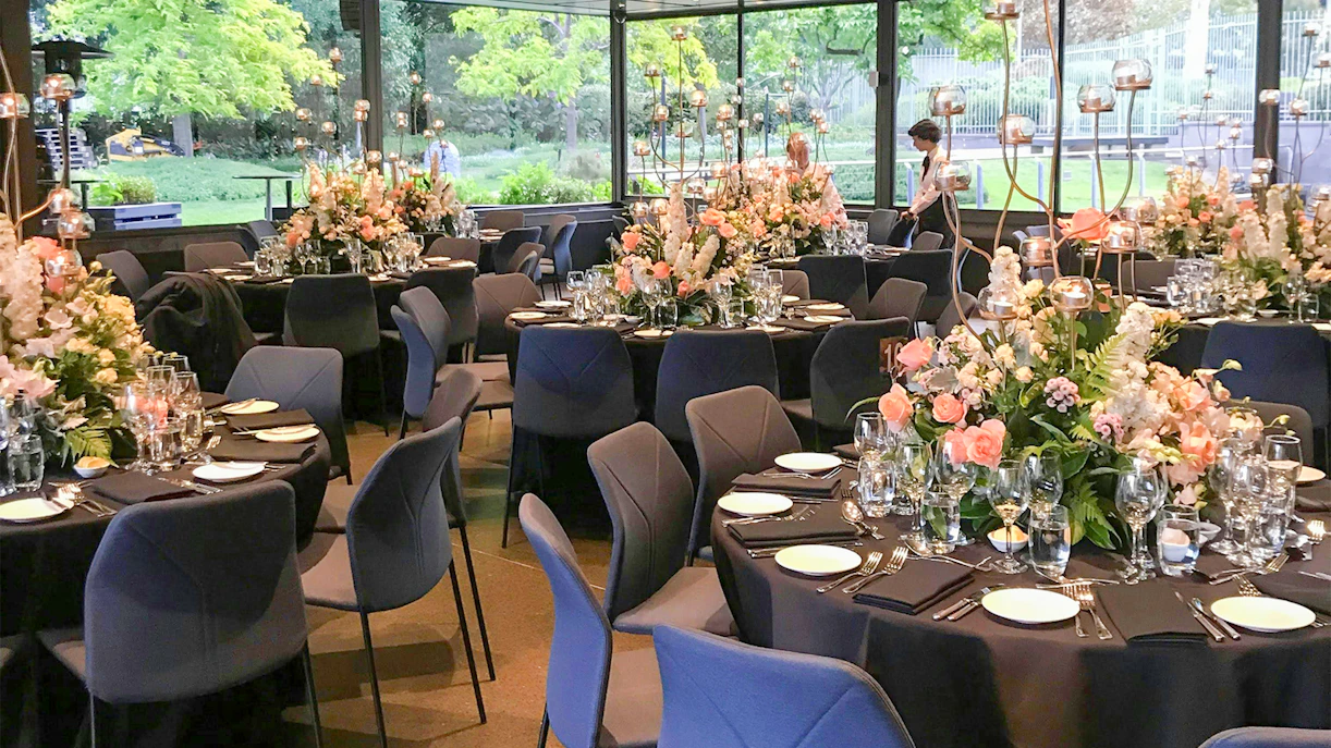NGV garden restaurant interior with tables set and floral decorations.