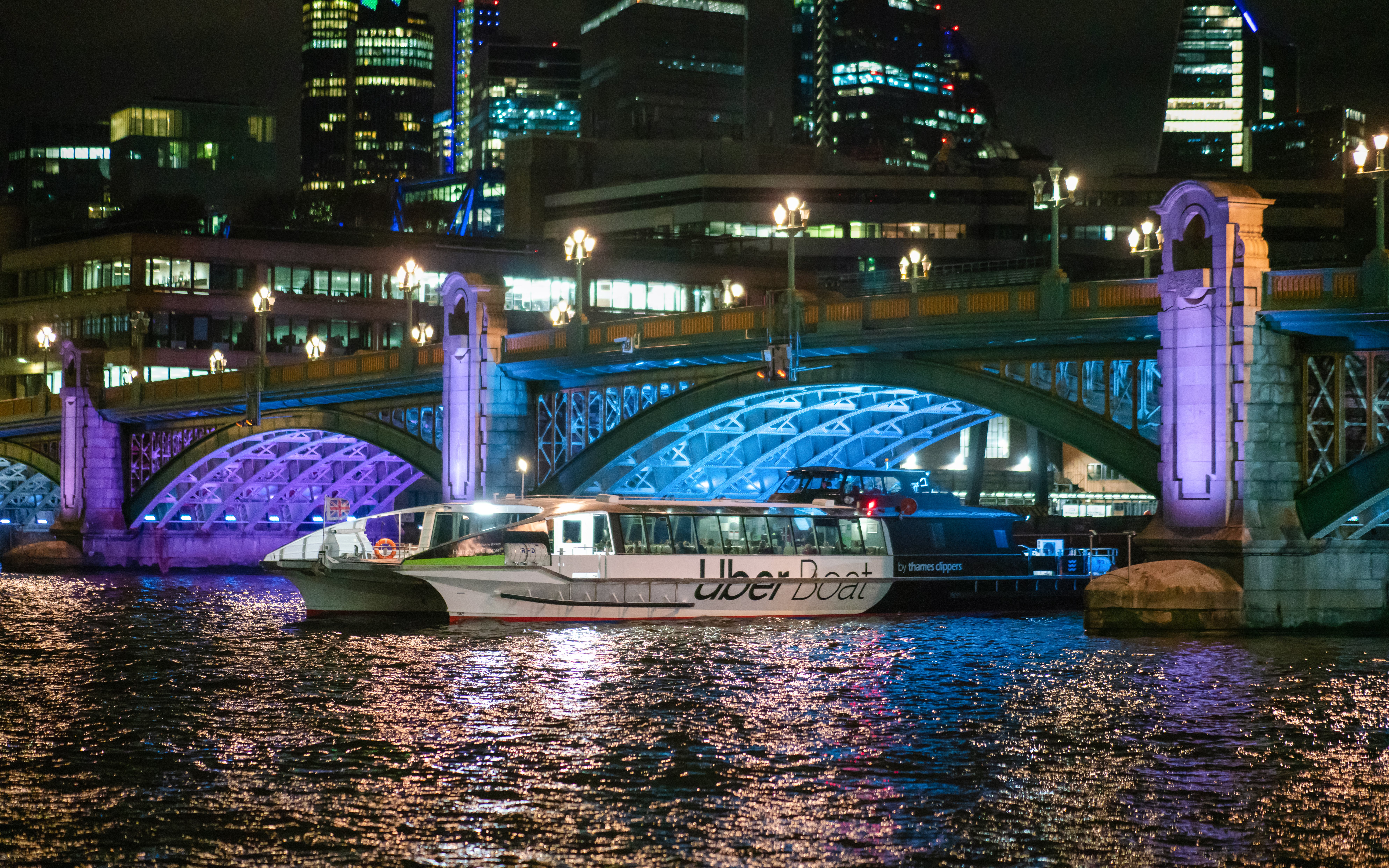 Uber Boat on River Thames at night with illuminated bridge and city skyline.
