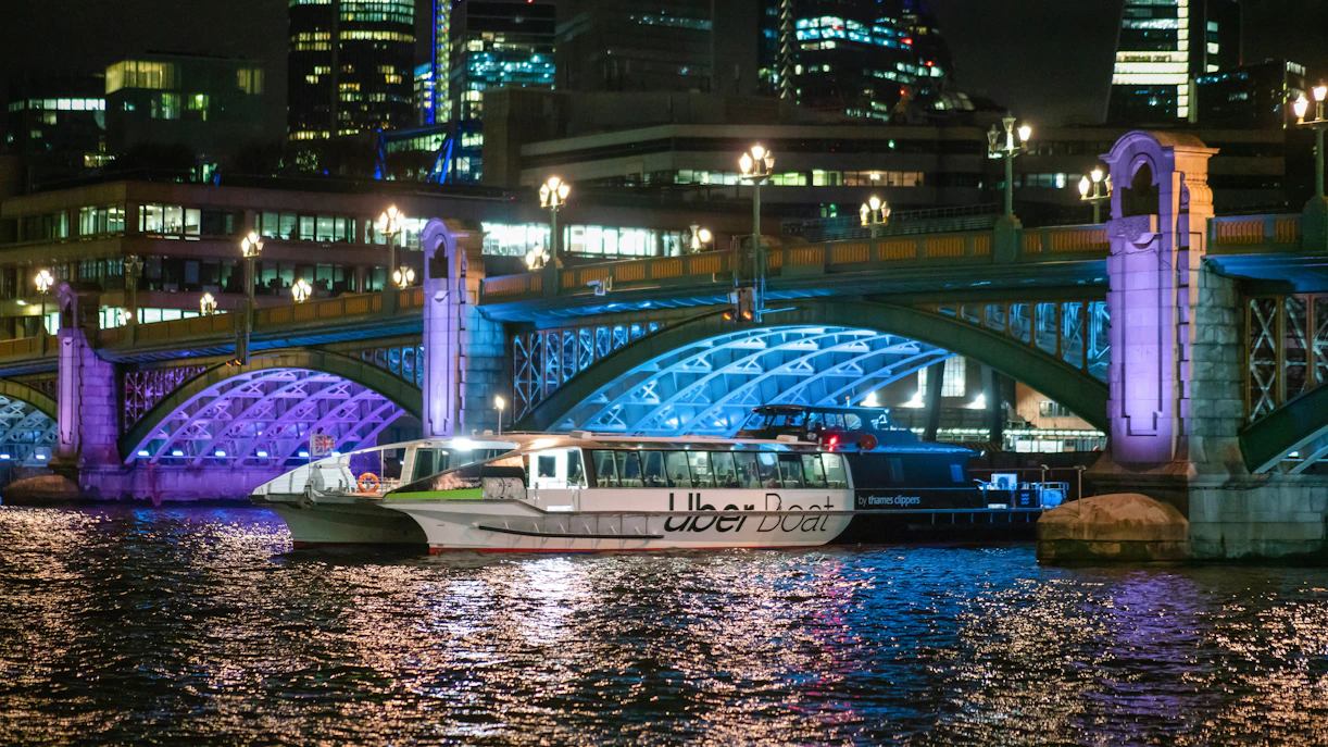 Uber Boat on River Thames at night with illuminated bridge and city skyline.