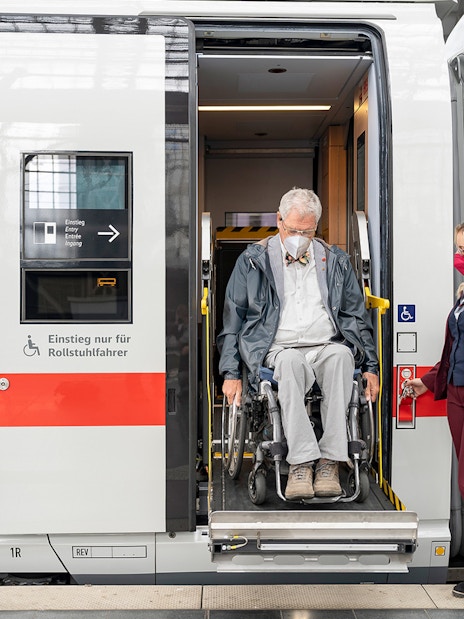 Man in wheelchair exiting train with assistance in Germany.