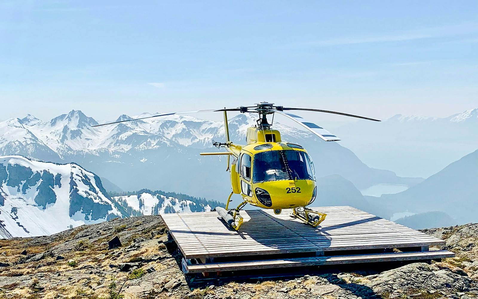 Yellow helicopter on a glacier landing pad with snowy mountains in Juneau.