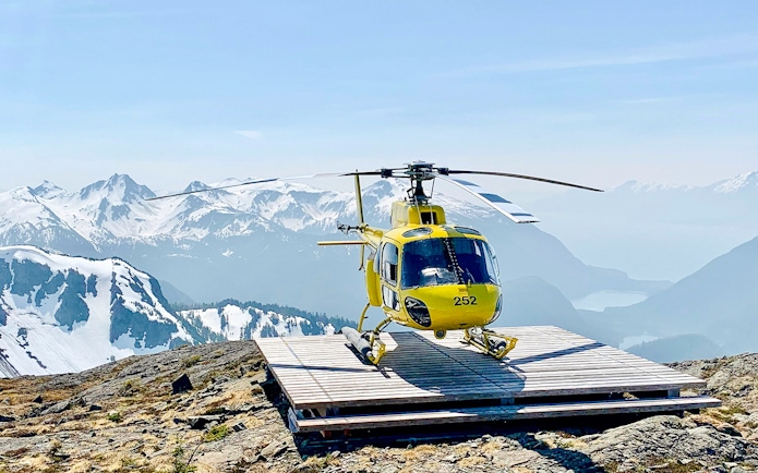 Yellow helicopter on a glacier landing pad with snowy mountains in Juneau.