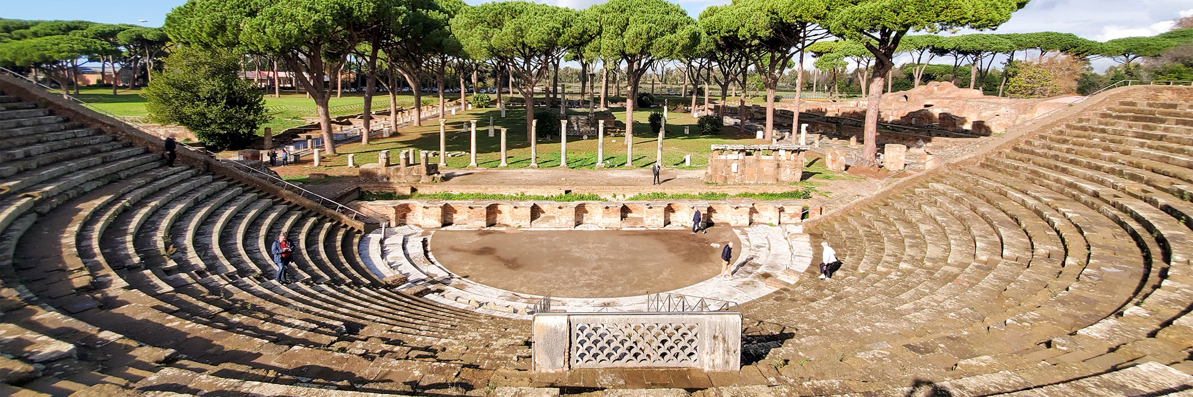 Ancient Roman theater in Ostia Antica with stone seating and surrounding trees.