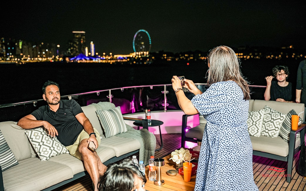 Tourists capturing night views on Superyacht TriDeck Cruise with city skyline.
