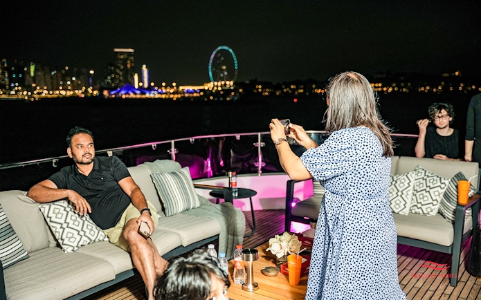 Tourists capturing night views on Superyacht TriDeck Cruise with city skyline.