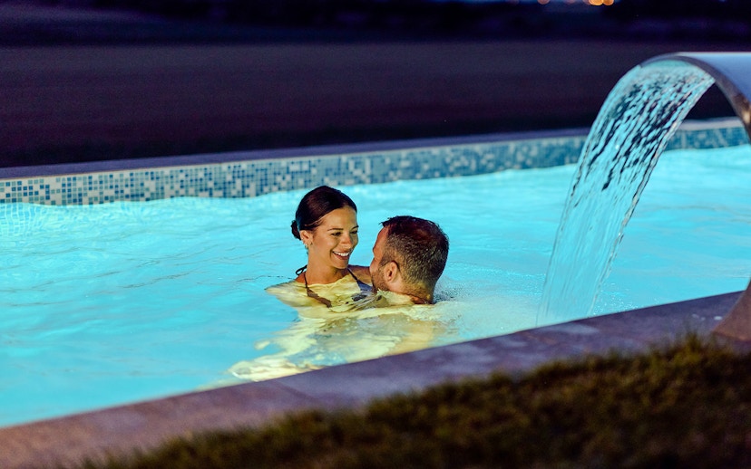 Couple enjoying a pool at twilight with water feature.