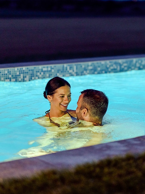 Couple enjoying a pool at twilight with water feature.
