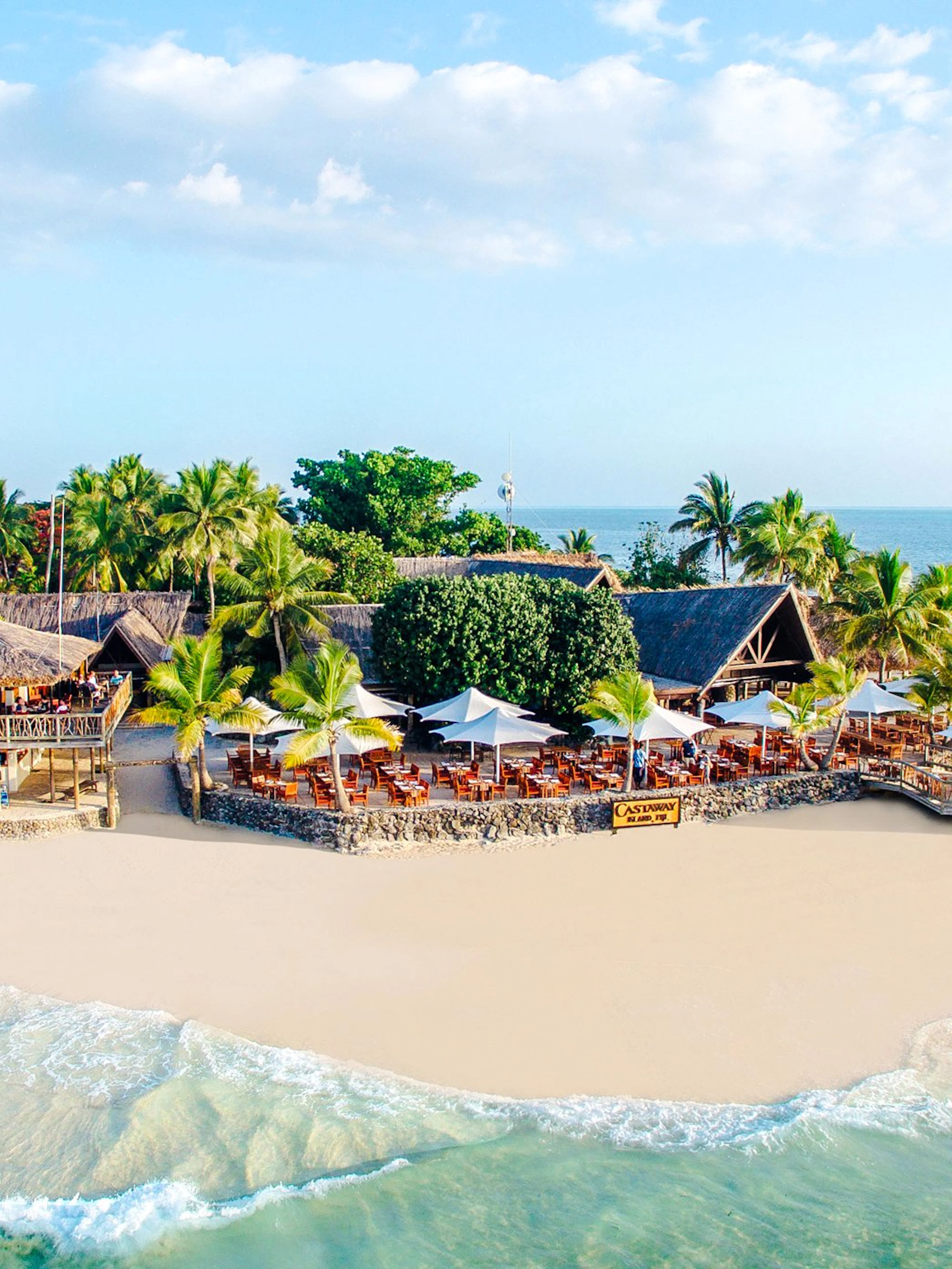 Aerial view of beachfront resort on Castaway Island, Fiji with palm trees and ocean.